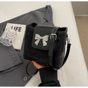 Detail of black bucket bag featuring silver bow ornament and matte leather texture