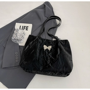 Detail of black tote bag featuring liquid metal butterfly ornament and pleated leather texture