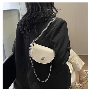 Close-up of a mini cream saddle bag with silver chain strap worn on a black blazer