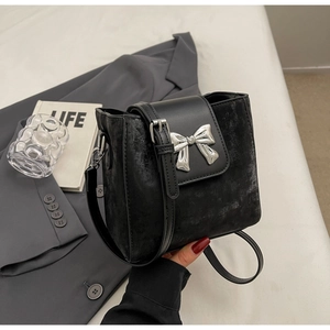 Detail of black bucket bag with silver metal bow and mixed leather texture