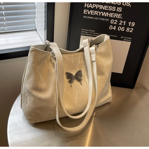 Detail of cream tote bag featuring a silver butterfly buckle on textured faux leather surface