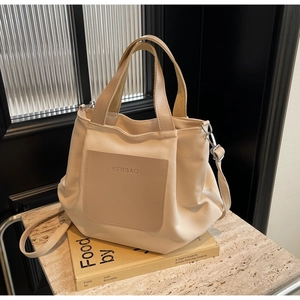 Détail d'un sac bandoulière beige clair avec écusson en cuir sur livre et pierre