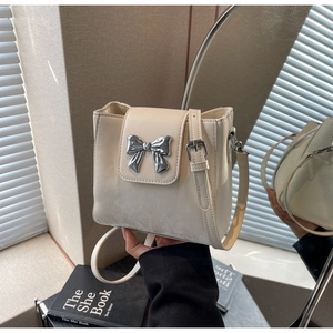 Detail of cream white leather bucket bag featuring a silver metal bow accent decoration