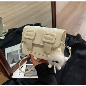 Detail of a cream crossbody bag with double buckle straps and a white plush monster charm