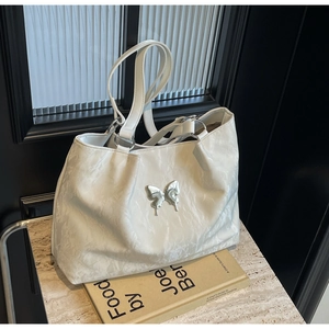 Detailed view of silver butterfly emblem on white pleated faux leather tote bag