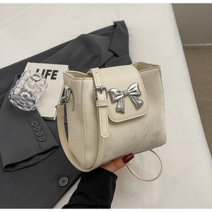 Detailed macro view of cream square bucket bag with silver bow buckle and faux leather texture