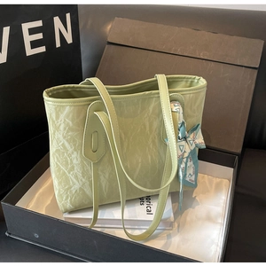 Close-up of light green tote bag with pleated texture and decorative silk scarf in gift box