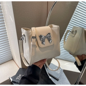 Detail of cream bucket bag showing silver metal bow clasp and textured vegan leather