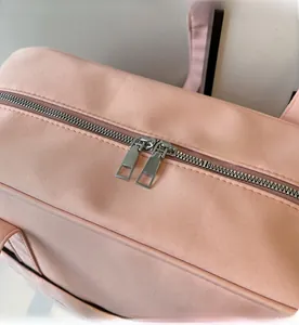 Detailansicht der glatten Metall-Doppelreißverschlüsse an einer rosa Reisetasche aus Canvas