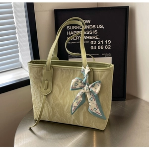 Detail of light green pleated tote bag featuring a decorative silk scarf on the metal table