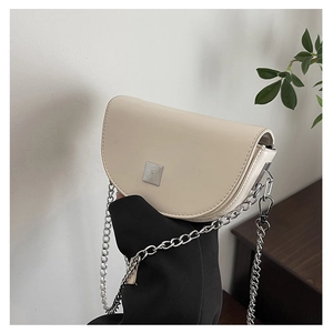 Detail of a creamy white saddle bag featuring a square metal clasp and silver chain strap