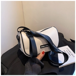 Detail of white cylinder crossbody bag with contrast black trim and wide fabric strap