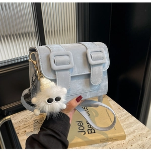 Detail of light blue crossbody bag featuring matte texture and plush eye bag charm