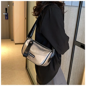 Detail of silver metallic cylinder crossbody bag featuring pleated texture and lettered strap