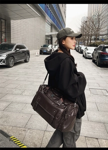 Detail of dark brown leather travel bag with dual handles and straps in city setting