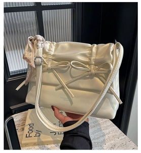 Detail of cream leather tote bag featuring bow accents and floral scarf wrapped on the handle