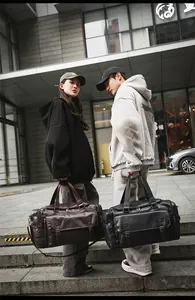 Close-up of brown and black leather duffel bags with adjustable straps in a street setting