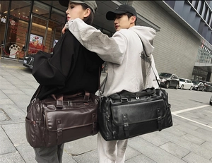 Detail of large travel bags in dark brown and black leather with adjustable shoulder straps