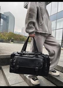 Detail of black large travel bag showing textured leather material and buckle pocket