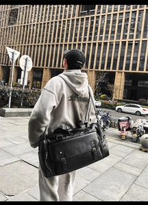 Rear view of model carrying a large black PU leather travel duffel bag in an urban street