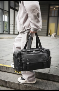 Macro shot of black leather travel bag featuring dual front buckle pockets and large capacity