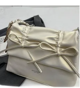 Close-up of cream leather shoulder bag with decorative bows and silk scarf handle detail