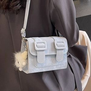 Light blue square crossbody bag with decorative buckles and a cute bear charm on model