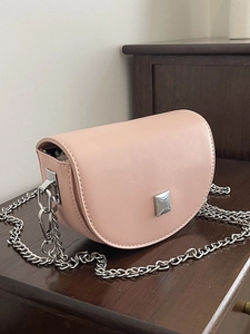 Mini light pink saddle bag with silver chain strap and metal buckle on wooden surface