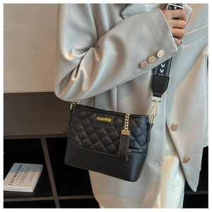 Detail of black quilted bucket bag with gold logo and patterned wide fabric strap
