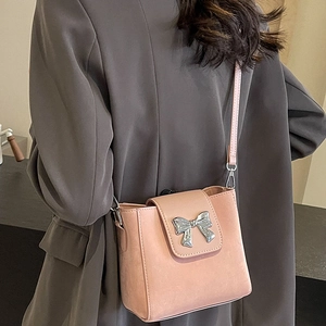 Pink crossbody bucket bag with silver bow buckle worn over a grey blazer jacket