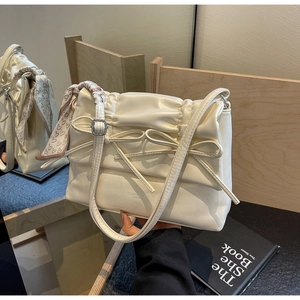 Detail of cream leather tote bag with bow accent and patterned silk scarf handle