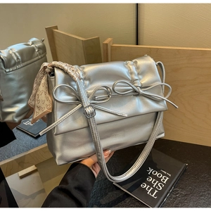 Detailed close-up of a silver quilted crossbody bag with decorative bows and floral silk scarf