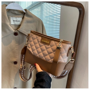 Close-up of beige quilted crossbody bag with brown leather trim and wide woven strap