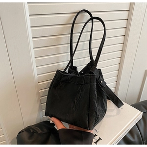 Dettaglio borsa a secchiello nera con texture increspata, manici sottili e tracolla