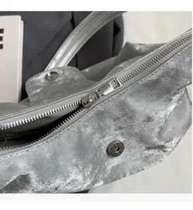 Détail macro du sac cabas argenté avec fermeture éclair fluide et bouton magnétique