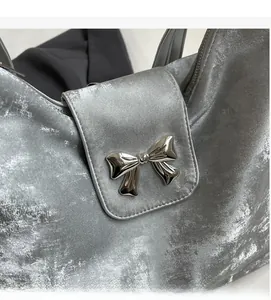 Gros plan sur la texture velours métallique et le nœud argenté du sac fourre-tout gris