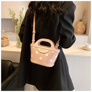 Pink polka dot handbag with adjustable strap shown from behind on a model's shoulder