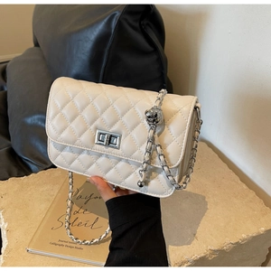 Detail der beigen Stepptasche mit silbernem Drehverschluss und Metallkugelkette