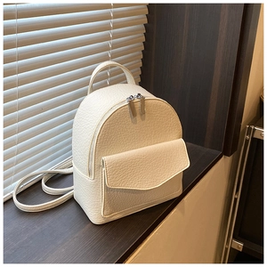 Detail of cream-white ruched backpack with lychee texture and silver zippers on wood