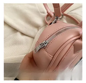 Close-up of pink round crossbody bag with silver zipper and cat ear stitching details
