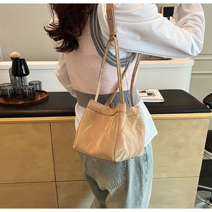Vista dettagliata della borsa a secchiello beige con trama a pieghe lucida e tracolle