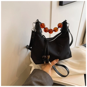 Detail of black crescent shoulder bag with amber beaded handle and geometric embroidery