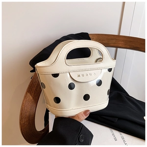 Detail of cream bucket bag with black polka dots and gold brand lettering