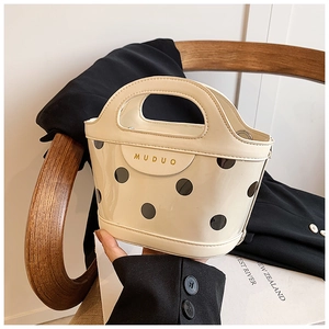 Detail of a creamy white glossy leather handbag with black polka dots on a wooden chair