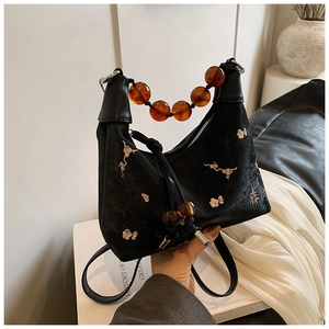Detail of black velvet baguette bag with gold floral embroidery and amber beaded handle