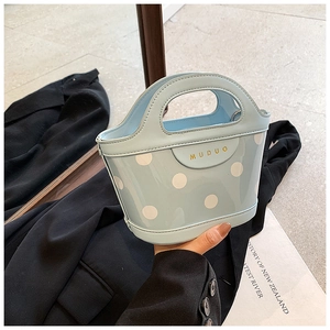 Close-up of light blue polka dot bucket bag with integrated oval handle and gold logo