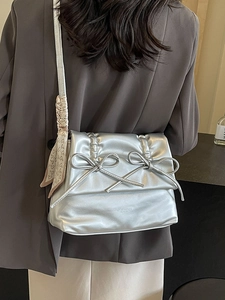 Metallic silver tote bag with bows and scarf accessory shown on a model in a grey suit