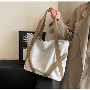 Detail of canvas tote bag showing brown crossover webbing straps and high texture finish