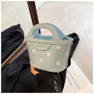 Close-up of light blue polka dot bucket bag with gold MUDUO logo and smooth handle