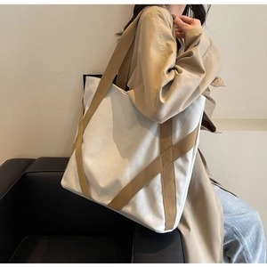 Detail of canvas tote bag with contrast brown straps shown on a beige trench coat